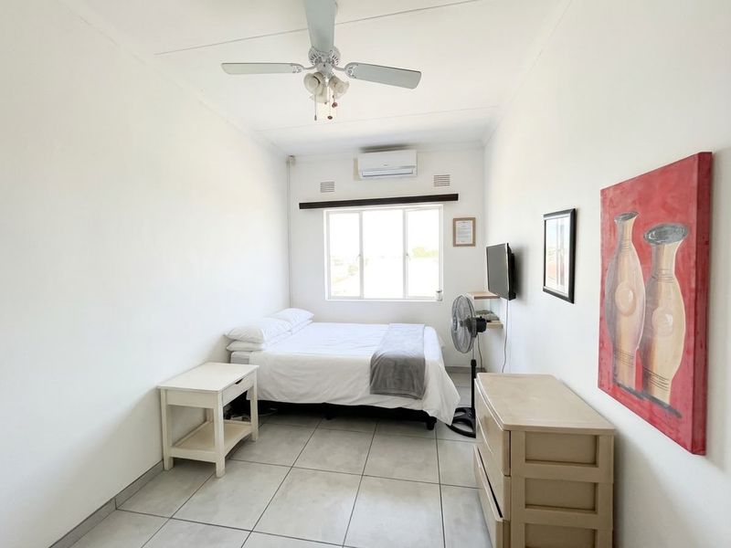 A functional bedroom featuring tiled flooring, a ceiling fan, and a wall-mounted split-system air conditioner.