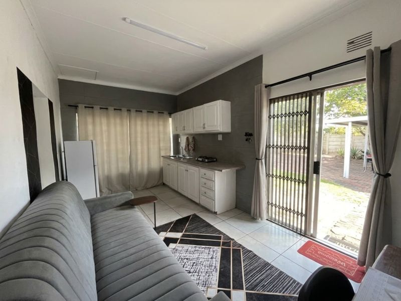 Open-plan living area featuring a compact kitchenette with built-in cabinetry, hob, and sink, with direct access to the outdoor patio through a sliding door.