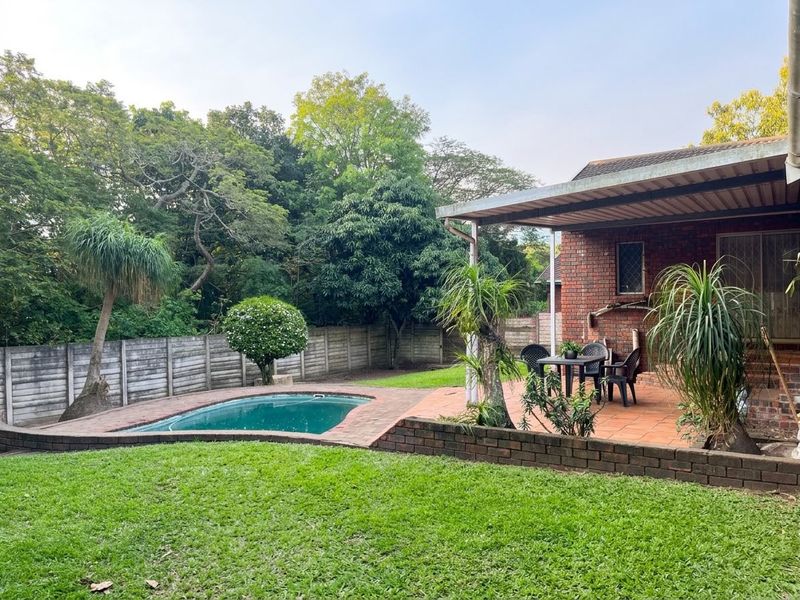 Rear garden featuring a swimming pool, paved patio area, and established lawn, enclosed by a perimeter wall.