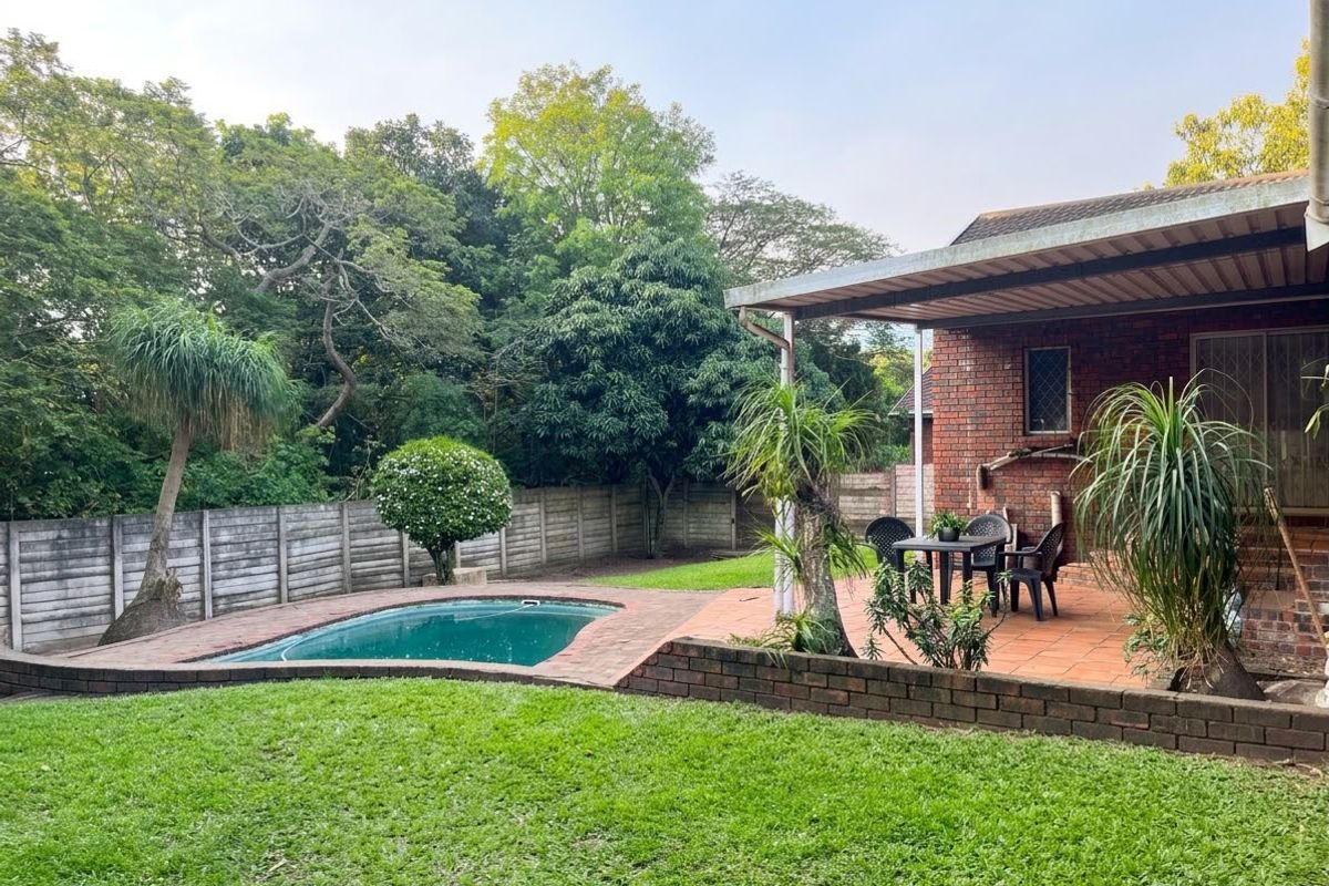 Rear garden featuring a swimming pool, paved patio area, and established lawn, enclosed by a perimeter wall.