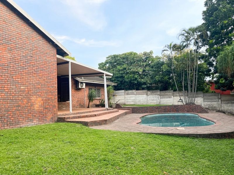 Rear garden featuring a swimming pool, paved patio area, covered veranda, and established landscaping enclosed by a precast concrete boundary wall.