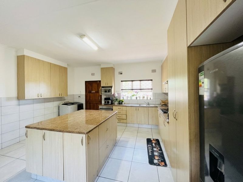 A functional kitchen featuring light wood cabinetry, a central island with stone countertop, tiled flooring, and integrated cooking appliances.
