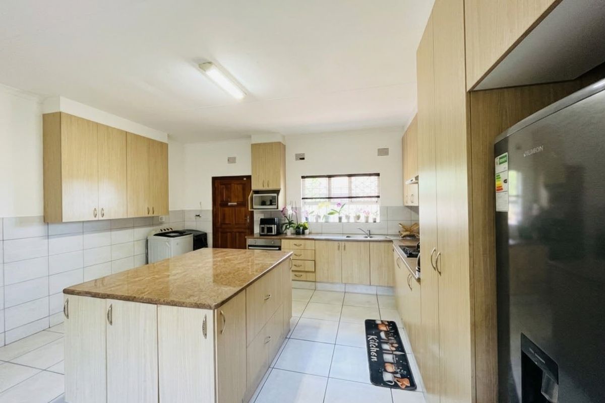 A functional kitchen featuring light wood cabinetry, a central island with stone countertop, tiled flooring, and integrated cooking appliances.