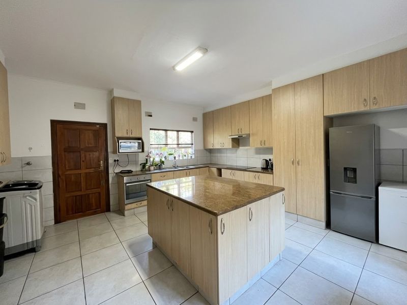 Spacious kitchen featuring light wood cabinetry, a central island with stone countertop, tiled flooring, and integrated appliances, offering a functional layout.