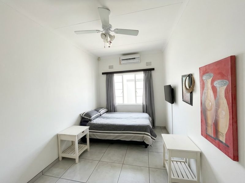 A functional bedroom featuring tiled flooring, a ceiling fan, and a wall-mounted air conditioning unit.