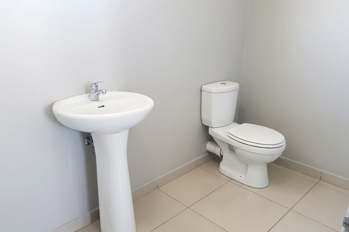 A clean and minimalist guest bathroom featuring a white pedestal basin with a chrome mixer tap and a matching ceramic toilet on tiled flooring.