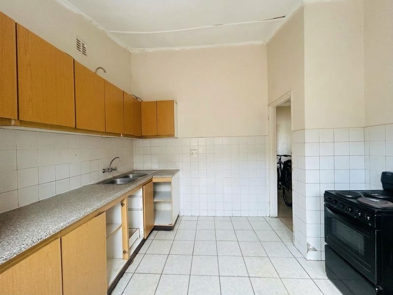 A dated kitchen featuring laminate cabinetry, tiled splashbacks, and a double sink, currently empty and requiring cosmetic updates to improve functionality and aesthetic appeal.