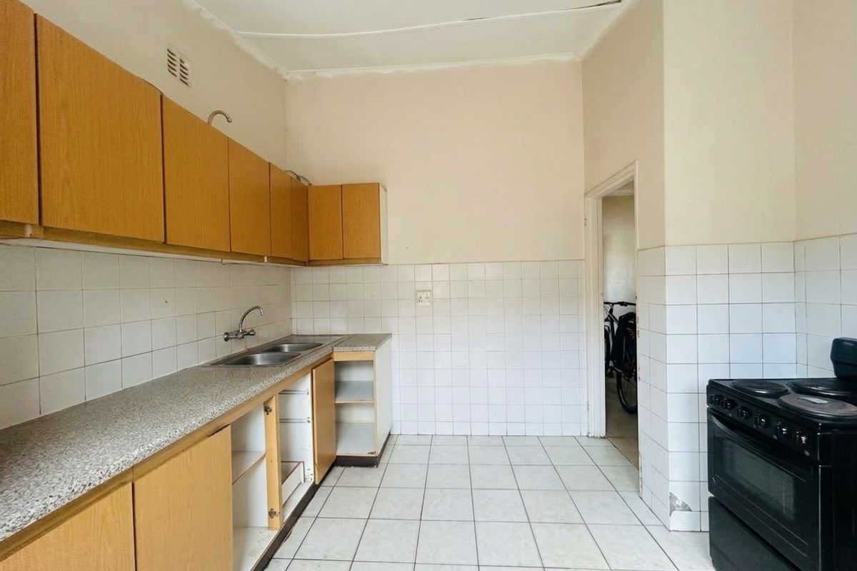 A dated kitchen featuring laminate cabinetry, tiled splashbacks, and a double sink, currently empty and requiring cosmetic updates to improve functionality and aesthetic appeal.
