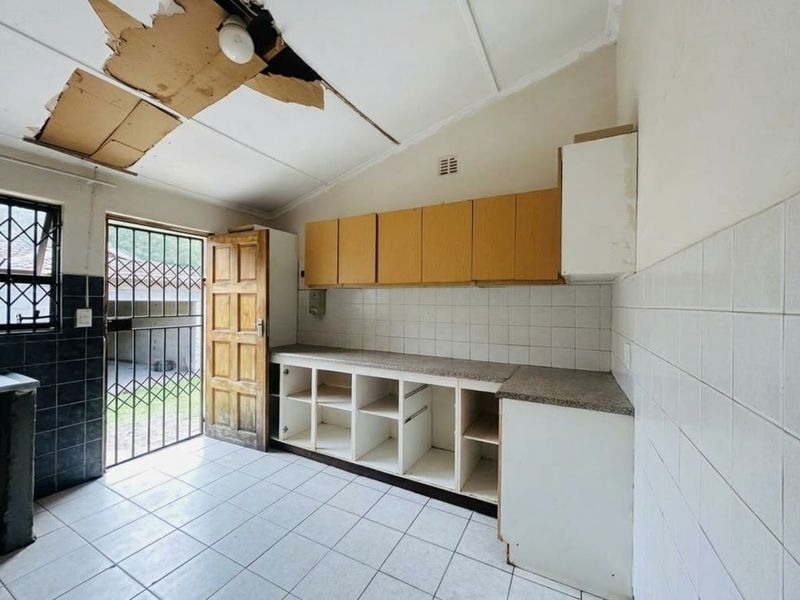 A kitchen space requiring renovation, featuring built-in cabinetry, tiled surfaces, and a security gate, with significant ceiling damage present.