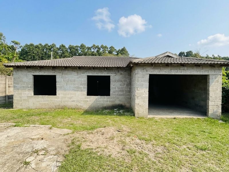 Rear view of an unfinished house structure featuring concrete block walls, a tiled roof, and an open garage bay.