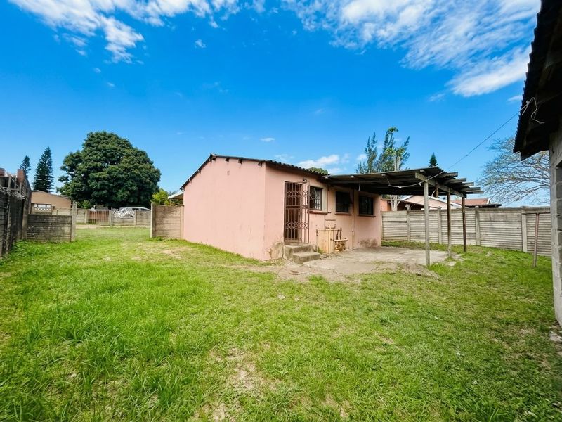 Rear view of the property featuring a small concrete patio with a timber pergola, enclosed by precast concrete boundary walls and a grassy yard.