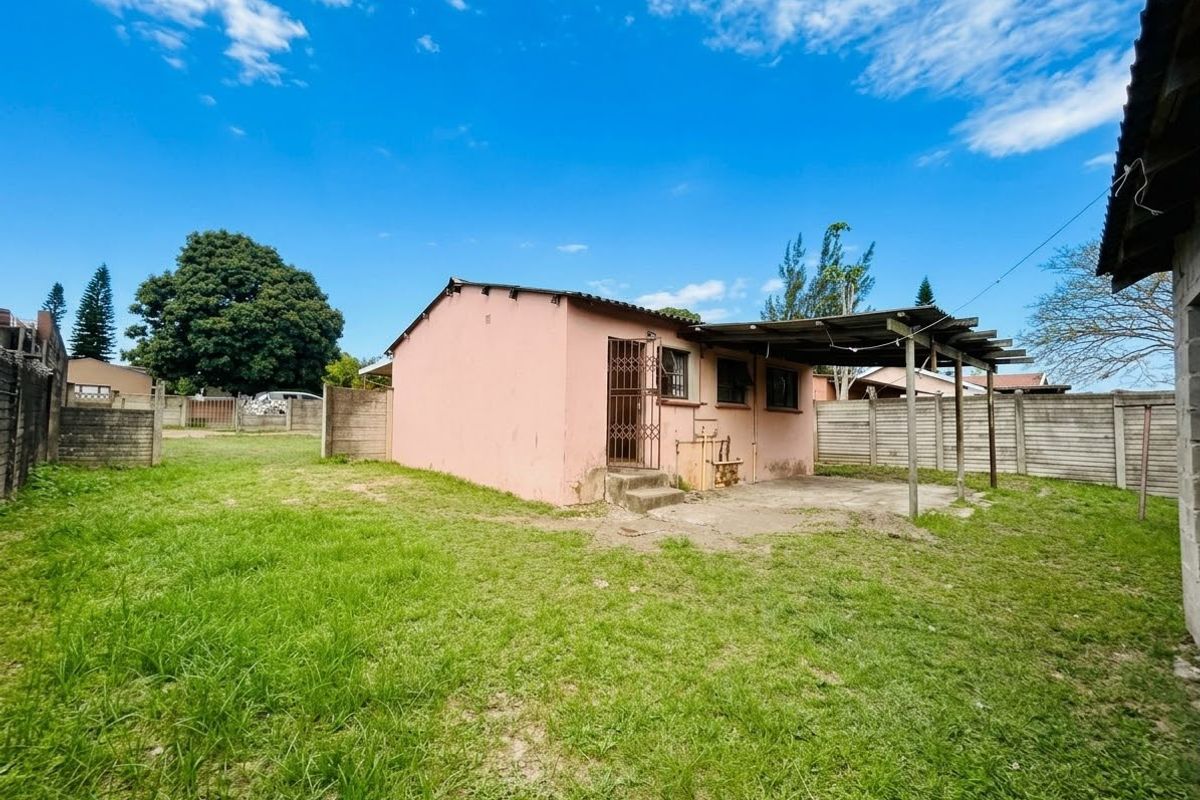 Rear view of the property featuring a small concrete patio with a timber pergola, enclosed by precast concrete boundary walls and a grassy yard.