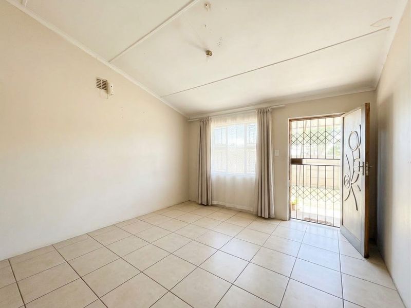 An empty living room featuring tiled flooring, a security gate at the entrance, and a window, providing a blank canvas for potential updates.