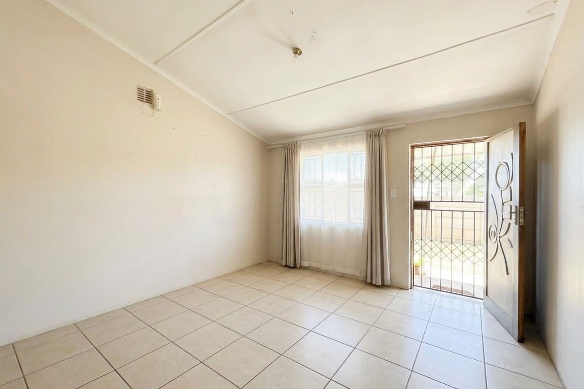 An empty living room featuring tiled flooring, a security gate at the entrance, and a window, providing a blank canvas for potential updates.