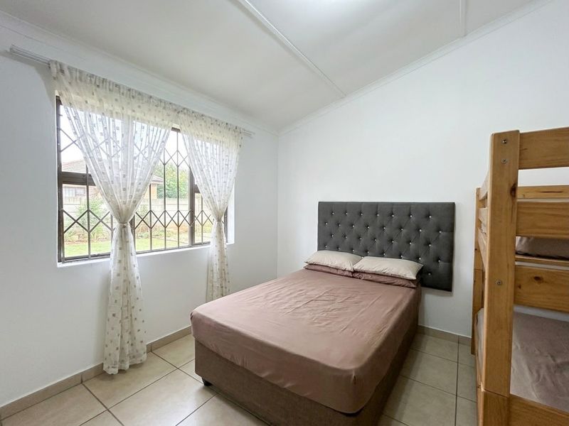 A functional bedroom featuring tiled flooring, a window with security bars, and neutral wall finishes, providing a clean and practical living space.
