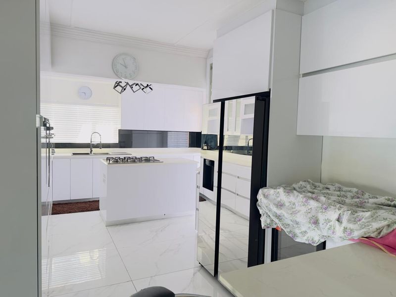 Modern kitchen featuring white cabinetry, a central island with a gas hob, marble-look floor tiles, and a sleek black glass splashback.