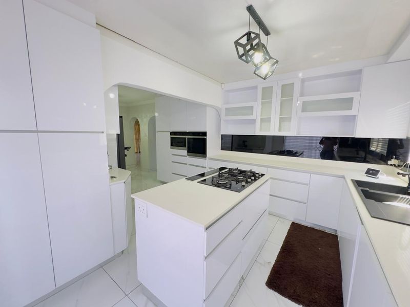 Modern, high-gloss white kitchen featuring a central island with a gas hob, built-in ovens, stone countertops, and sleek cabinetry.