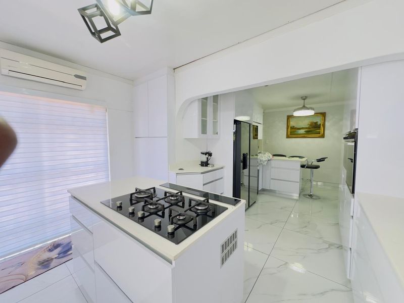 Modern open-plan kitchen featuring a central island with a gas hob, sleek white cabinetry, and polished marble-look floor tiles.