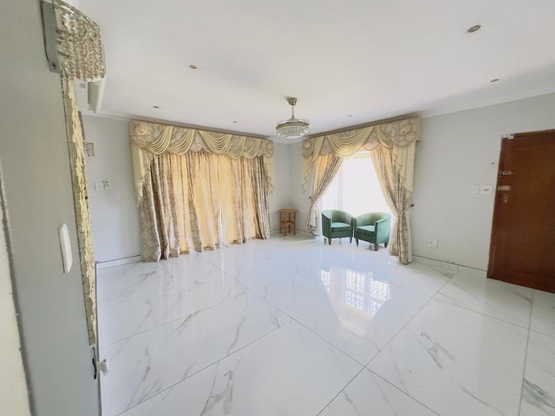 Spacious living room featuring polished marble-look porcelain floor tiles, recessed downlighting, and elegant decorative ceiling fixtures, offering a bright and modern living space.