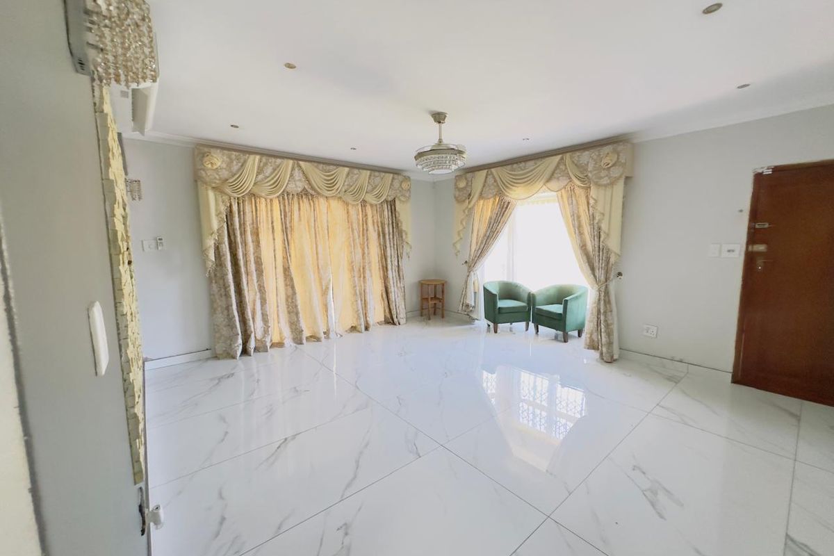 Spacious living room featuring polished marble-look porcelain floor tiles, recessed downlighting, and elegant decorative ceiling fixtures, offering a bright and modern living space.