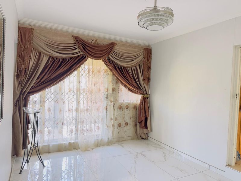 A bright and spacious living area featuring polished tiled flooring, a modern ceiling light fixture, and a sliding glass door with security gate.