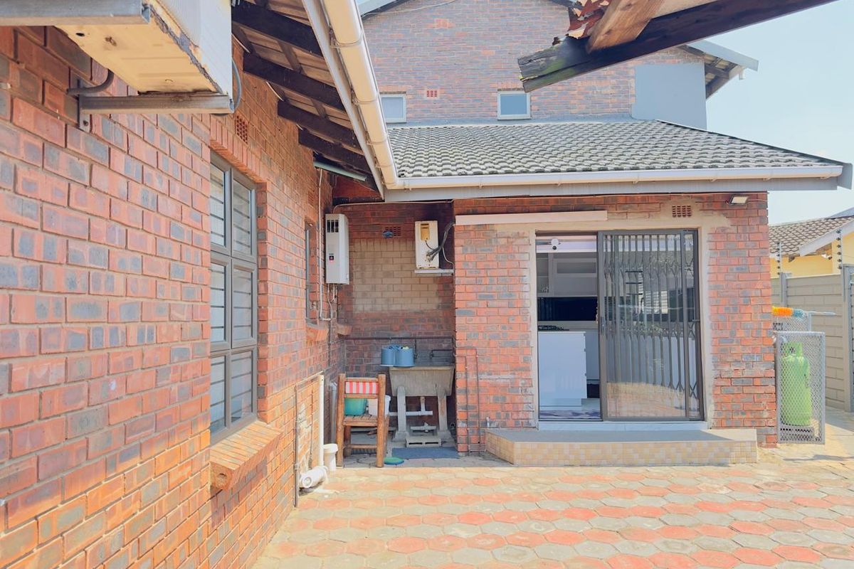 Rear exterior view of a face brick house featuring a paved patio area, utility sink, and sliding door access to the interior.