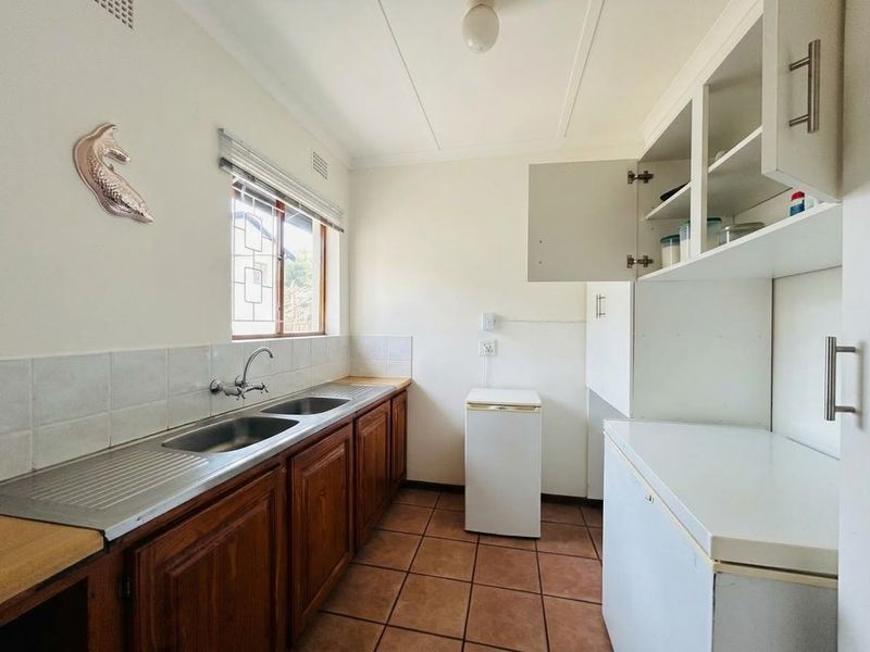 Functional scullery featuring wooden cabinetry, a double stainless steel sink, tiled flooring, and ample storage space, providing a practical utility area.