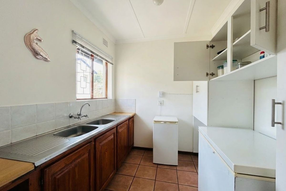 Functional scullery featuring wooden cabinetry, a double stainless steel sink, tiled flooring, and ample storage space, providing a practical utility area.