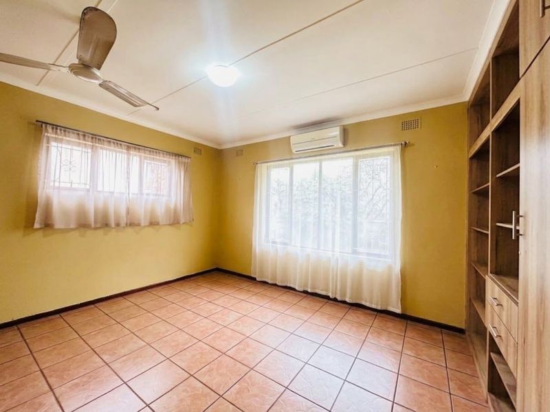 Spacious bedroom featuring tiled flooring, a built-in shelving unit, ceiling fan, and a wall-mounted air conditioning unit.