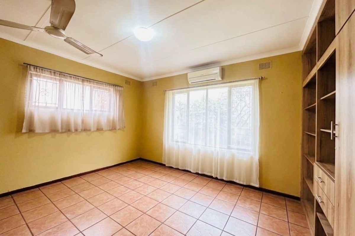 Spacious bedroom featuring tiled flooring, a built-in shelving unit, ceiling fan, and a wall-mounted air conditioning unit.