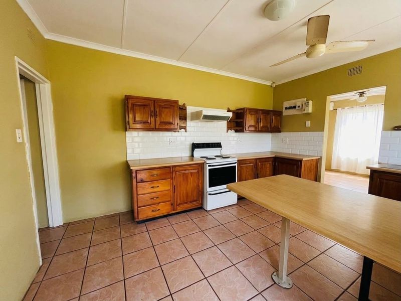A functional kitchen featuring wooden cabinetry, a tiled backsplash, and a freestanding stove, with tiled flooring throughout.