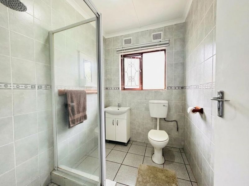 A functional bathroom featuring a glass-enclosed shower, a vanity basin, and a toilet, finished with neutral wall and floor tiling.