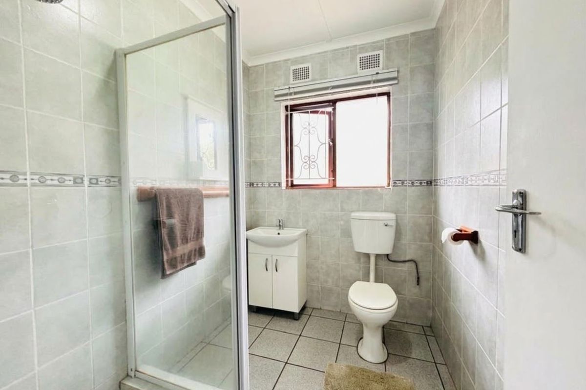 A functional bathroom featuring a glass-enclosed shower, a vanity basin, and a toilet, finished with neutral wall and floor tiling.