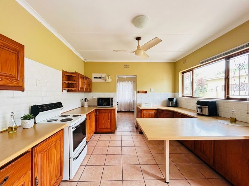 A functional kitchen featuring wooden cabinetry, subway tile backsplash, ceramic tiled flooring, and a ceiling fan, offering a classic layout with ample counter space.