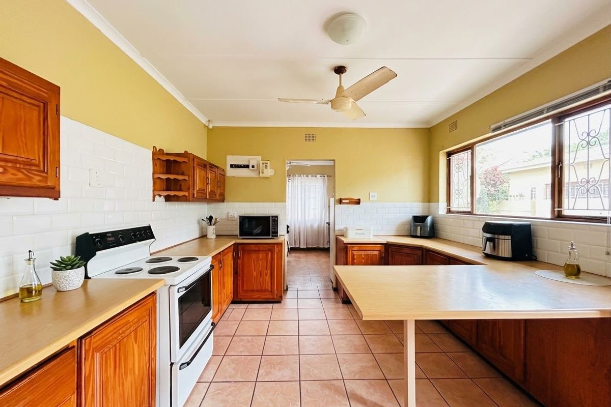 A functional kitchen featuring wooden cabinetry, subway tile backsplash, ceramic tiled flooring, and a ceiling fan, offering a classic layout with ample counter space.