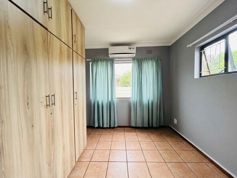 A clean, empty bedroom featuring light wood-finish built-in cupboards, tiled flooring, and a wall-mounted air conditioning unit.