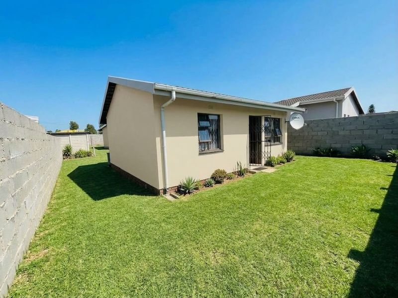 A view of the rear exterior of the house featuring a well-maintained lawn, concrete block boundary walls, and a secure entrance.