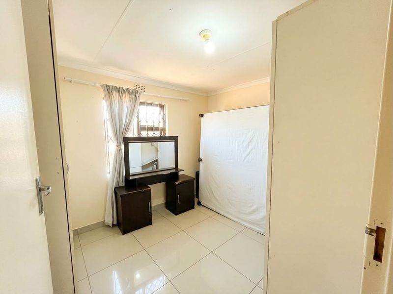 A bedroom featuring tiled flooring, a window with security bars, and a coved ceiling, offering a clean and functional space.