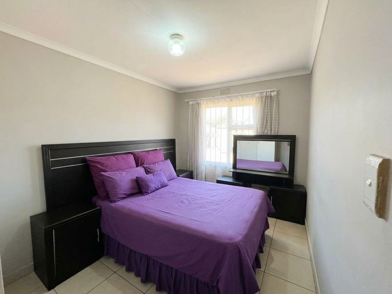A functional bedroom featuring tiled flooring, security bars on the window, and neutral wall finishes.