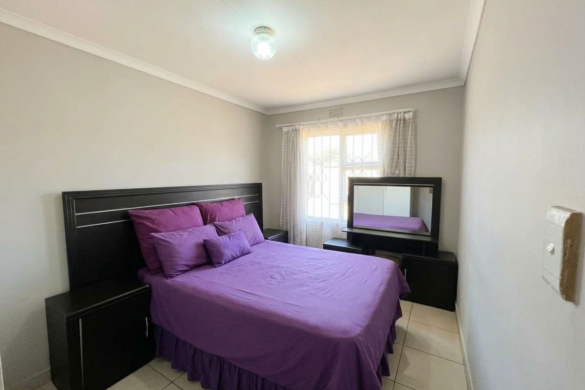 A functional bedroom featuring tiled flooring, security bars on the window, and neutral wall finishes.