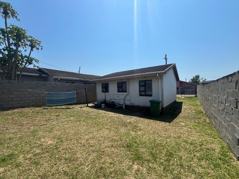 Rear view of the property featuring a small backyard enclosed by concrete block boundary walls and a simple tiled roof structure.
