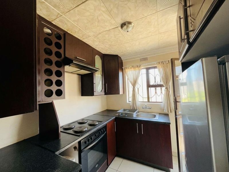 A functional kitchen featuring dark wood cabinetry, laminate countertops, integrated electric hob and oven, and a stainless steel sink.