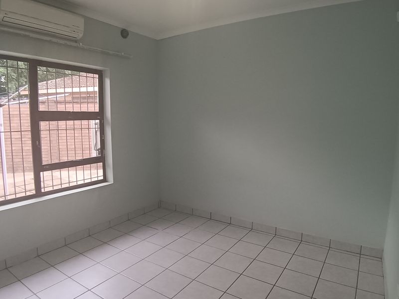 An empty bedroom featuring tiled flooring, a wall-mounted air conditioning unit, and a window fitted with security bars.