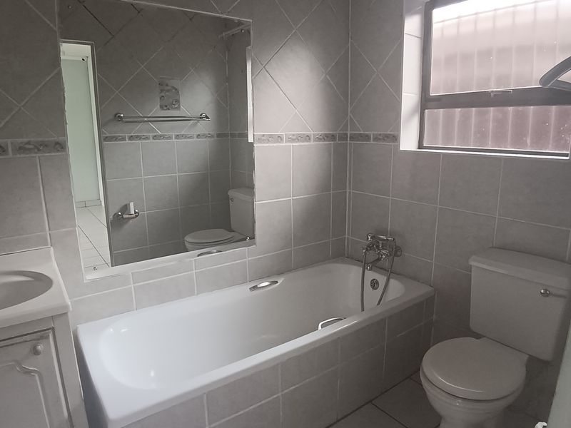 A functional bathroom featuring a bathtub, toilet, and vanity unit with tiled walls and flooring, offering a clean and practical layout.