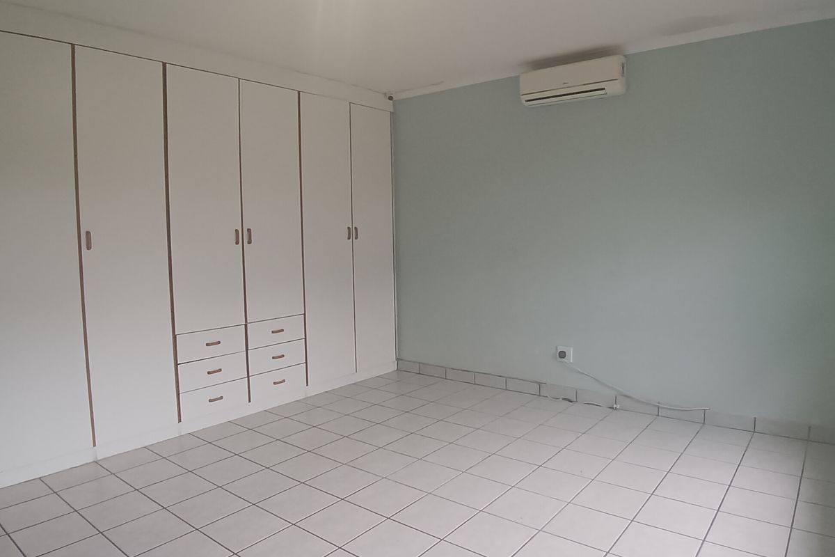 An empty bedroom featuring tiled flooring, extensive built-in cupboard storage, and a wall-mounted air conditioning unit.
