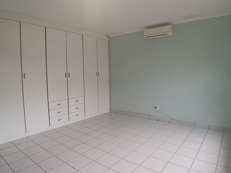 An empty bedroom featuring tiled flooring, extensive built-in cupboard storage, and a wall-mounted air conditioning unit.