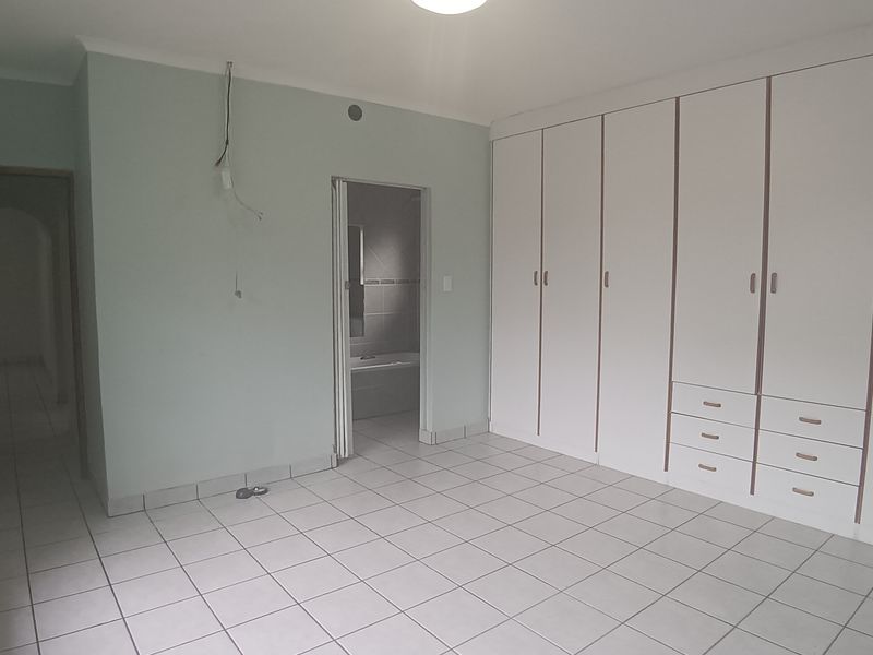 Spacious bedroom featuring neutral tiled flooring, extensive built-in cupboard storage, and direct access to an en-suite bathroom.
