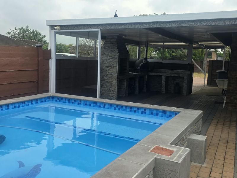 Outdoor entertainment area featuring a swimming pool with tiled coping and a covered patio equipped with a built-in braai and paved flooring.