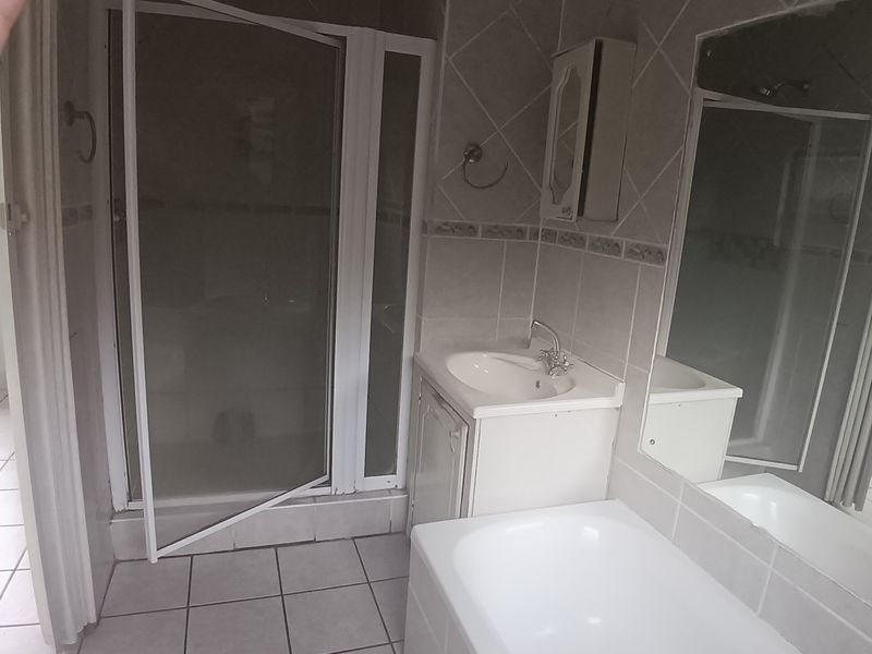 A dated bathroom featuring a shower enclosure, vanity basin, and bathtub with tiled finishes, currently requiring maintenance and cosmetic updates.