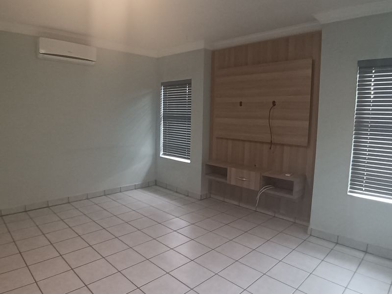 An empty living room featuring tiled flooring, a built-in media console, air conditioning, and venetian blinds.